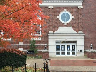 A rainy scene of the Science and Engineering Library front door, with a tree with brilliant fall colors to the left of the door.  There is a bike rack with a single bike parked out front of the library.